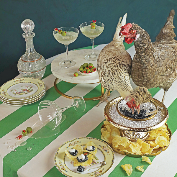 Two chickens on a table with drinks, snacks, and decorative elements.